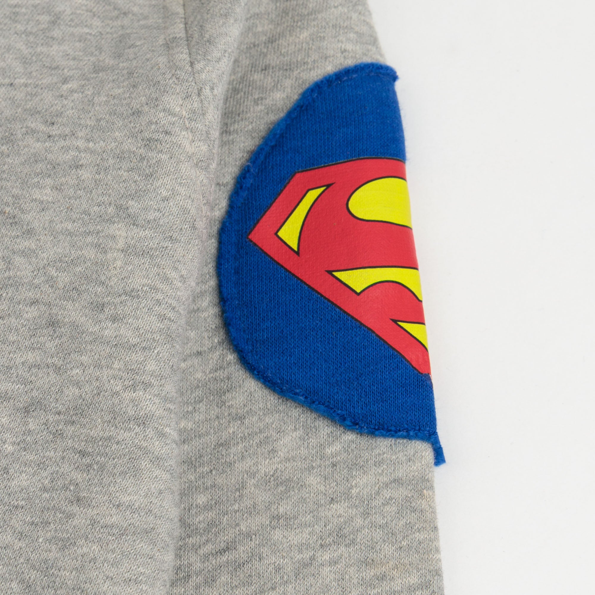 Close-up of the blue, red and yellow superhero patch on the sleeve of the grey boys’ hoodie.