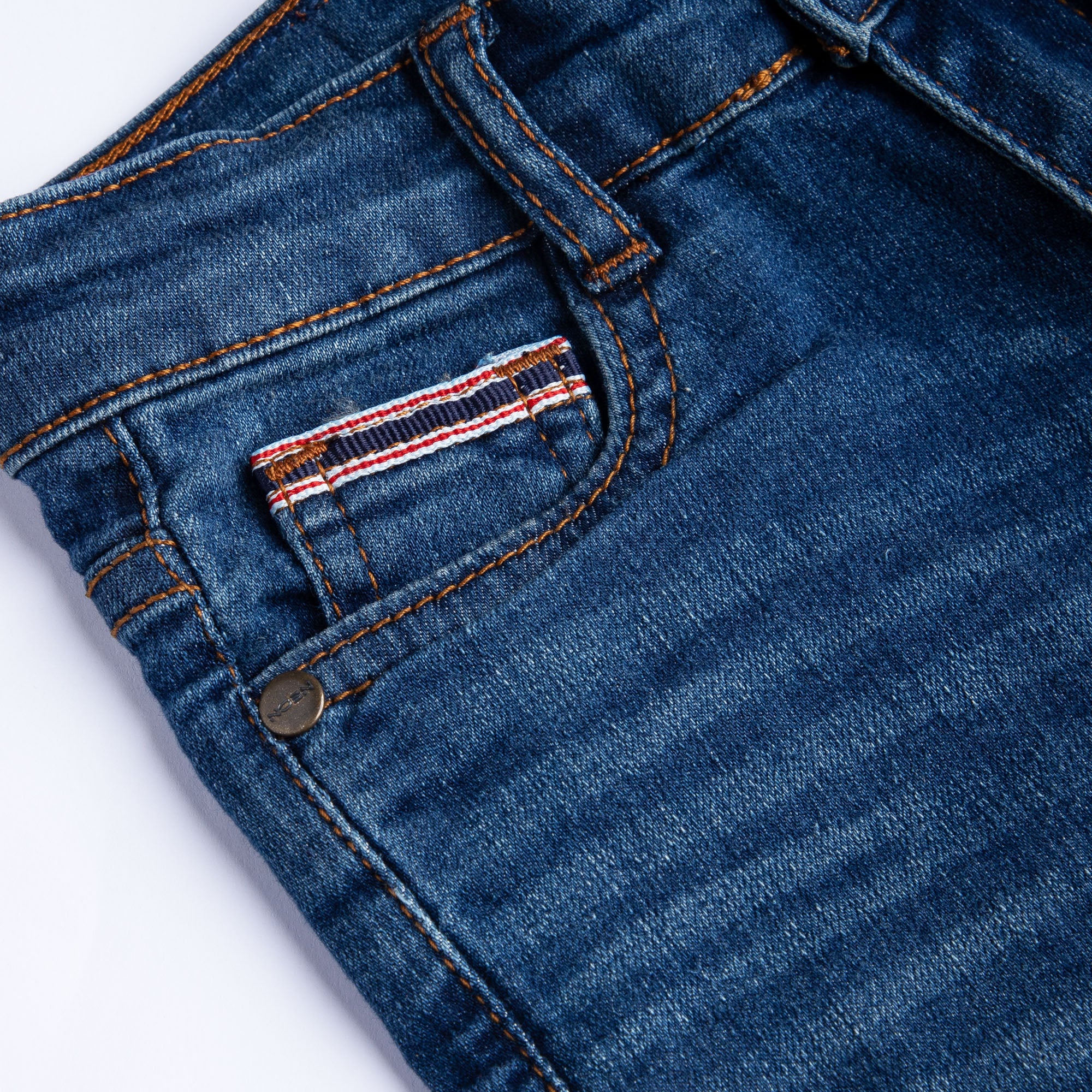 Close-up of the front coin pocket, striped fabric detail, metal rivet and faded finish on the kids dark wash denim.