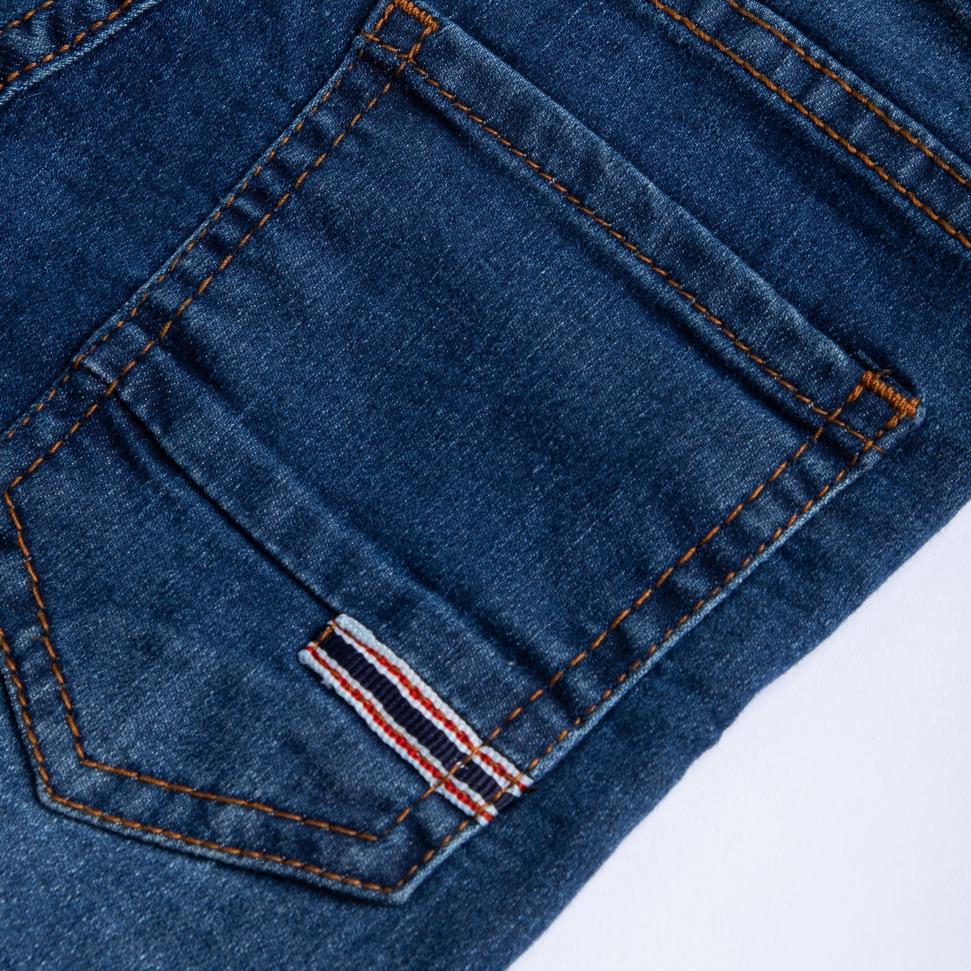 Close-up of the back pocket, contrast stitching and striped fabric detail on the kids dark wash denim.