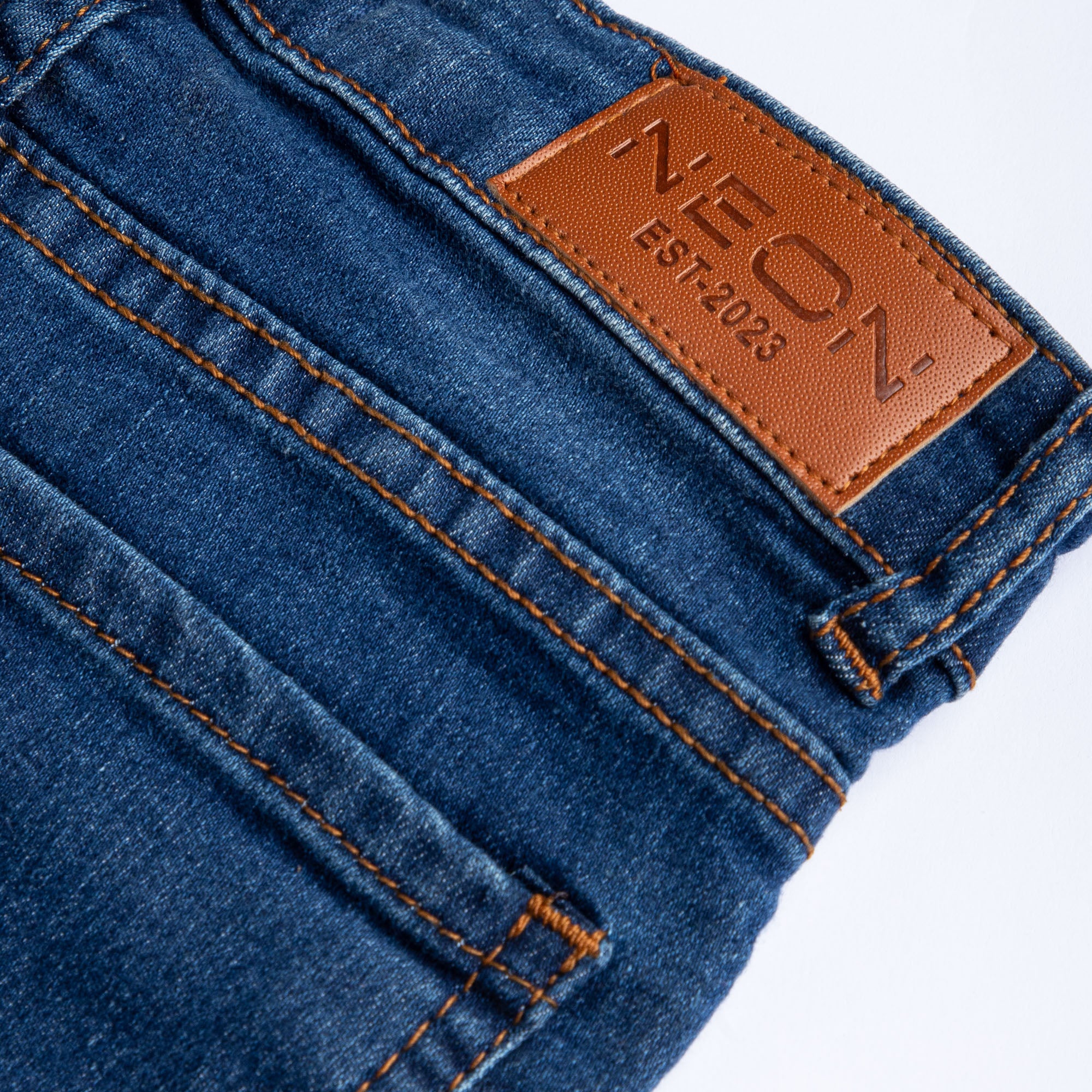 Close-up of the branded tan waist patch, belt loop and contrast stitching on the kids dark wash denim.