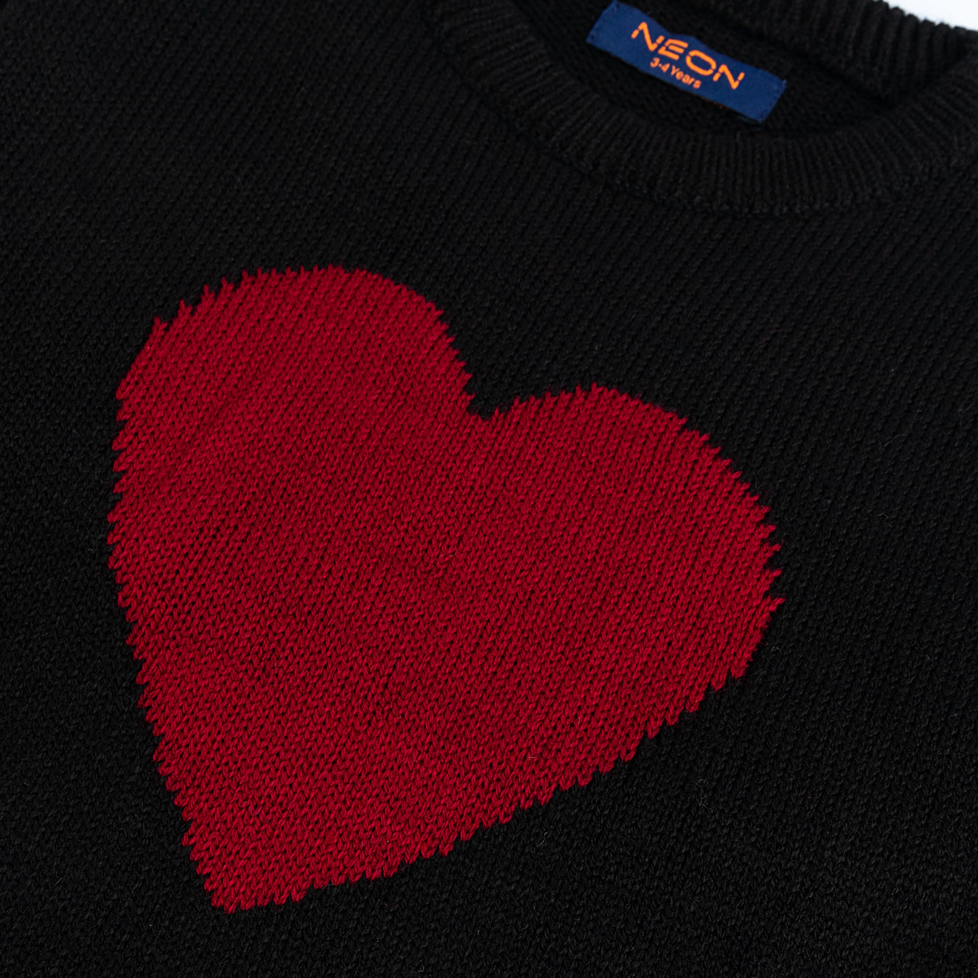 Close-up view of the bold red heart design and soft black cotton texture on the girls crew neck sweater.
