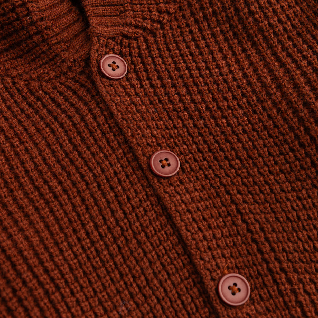 Close-up view of the rust brown textured acrylic fabric and matching front buttons on the girls hooded cardigan.