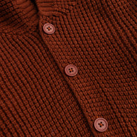 Close-up view of the rust brown textured acrylic fabric and matching front buttons on the girls hooded cardigan.