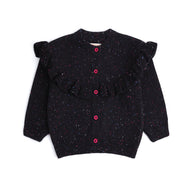 Front view of a black cotton cardigan for girls, featuring multicolor speckles, a statement ruffle across the shoulders and front, pink buttons and ribbed edges.