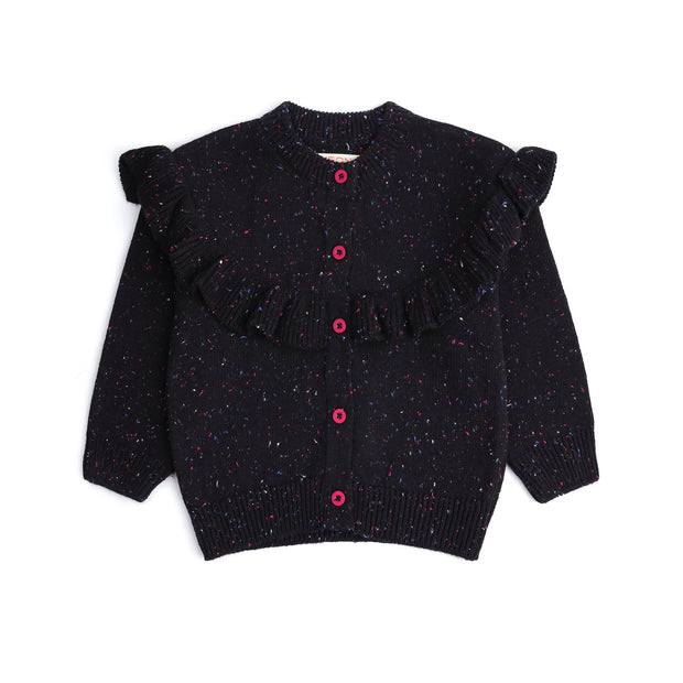 Front view of a black cotton cardigan for girls, featuring multicolor speckles, a statement ruffle across the shoulders and front, pink buttons and ribbed edges.