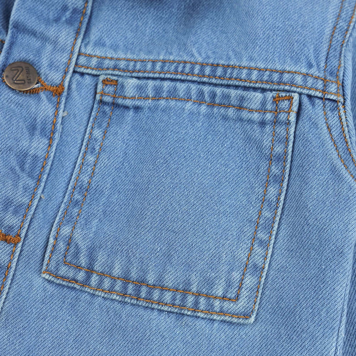 Close-up view of the light wash denim jacket showing its durable denim texture, chest pocket construction, contrast stitching and metal button detailing.