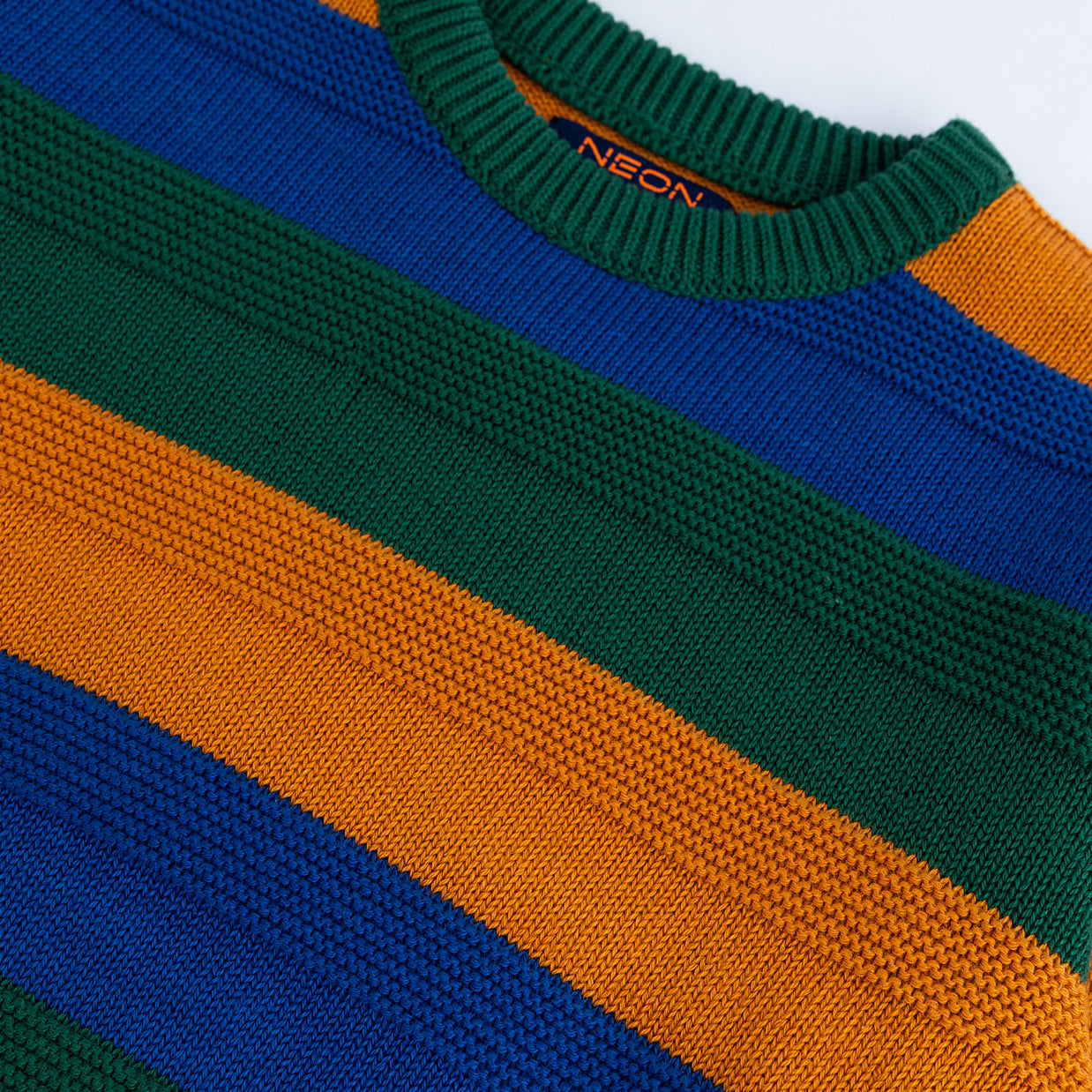 Close-up view of the green, royal blue and mustard cotton texture and ribbed crew neck on the boys striped sweater.