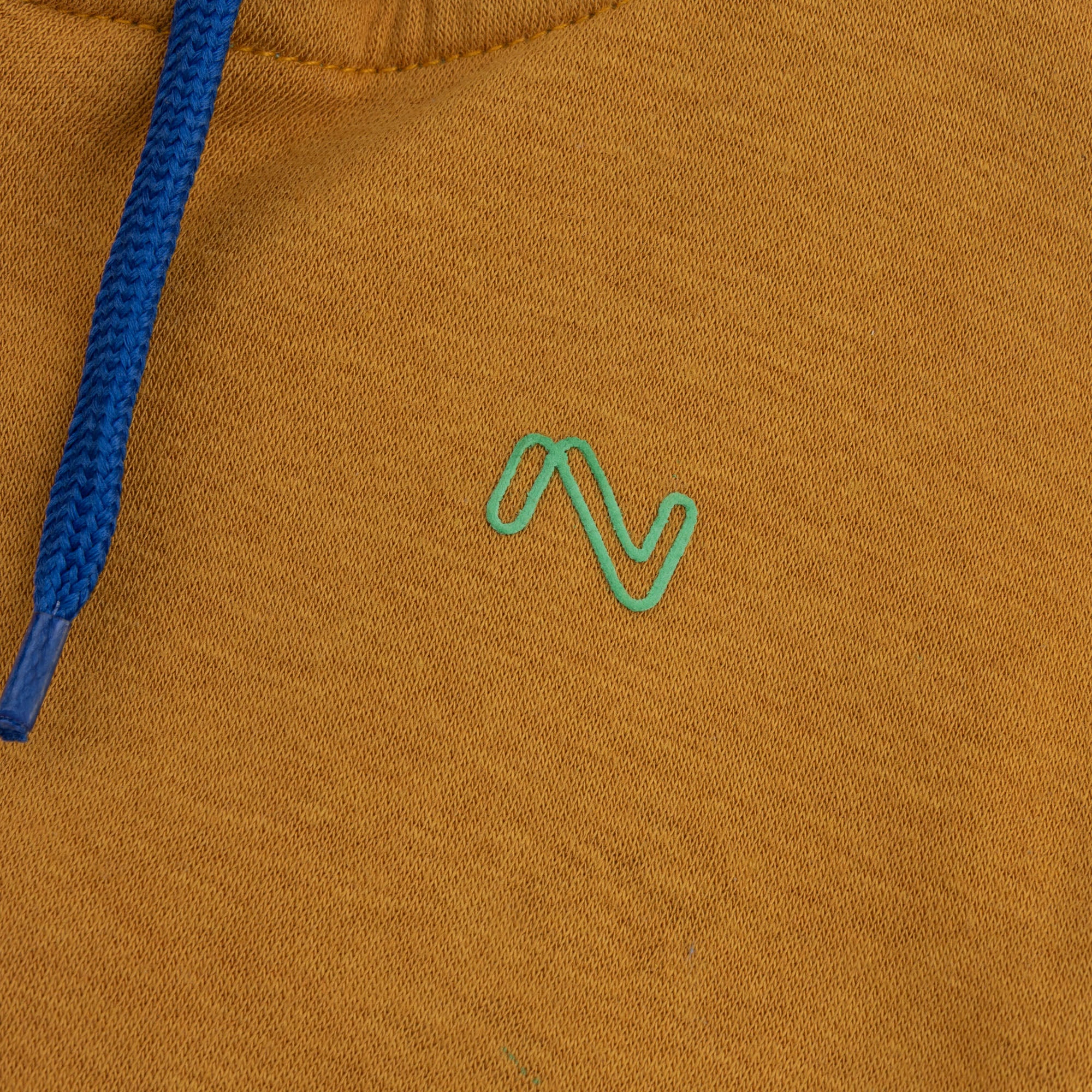 Close-up of the turquoise embroidered chest logo and contrast blue drawstring on the mustard fleece zip-up hoodie for kids.