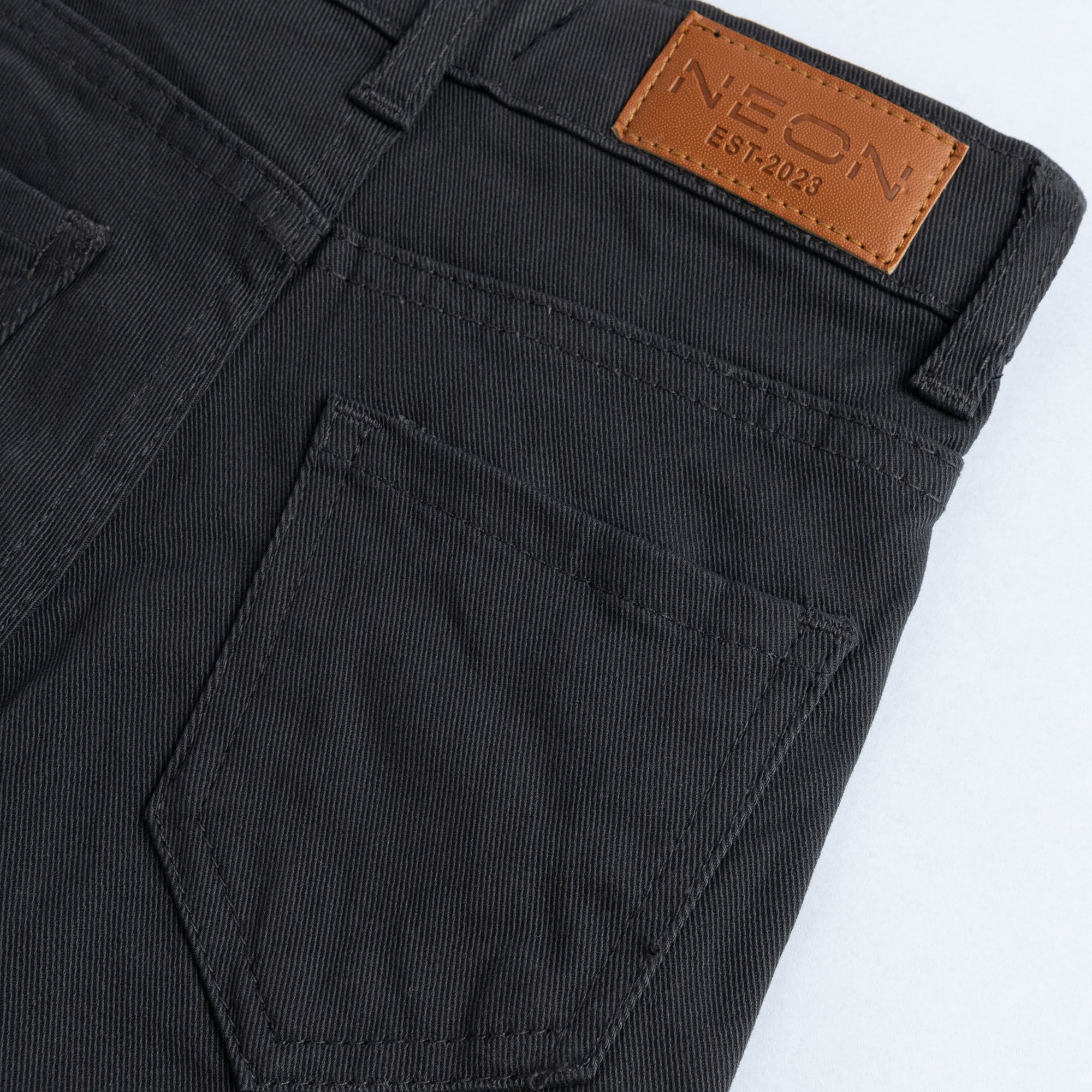 Close-up of the back pocket and branded tan waist patch on the kids charcoal twill pants.