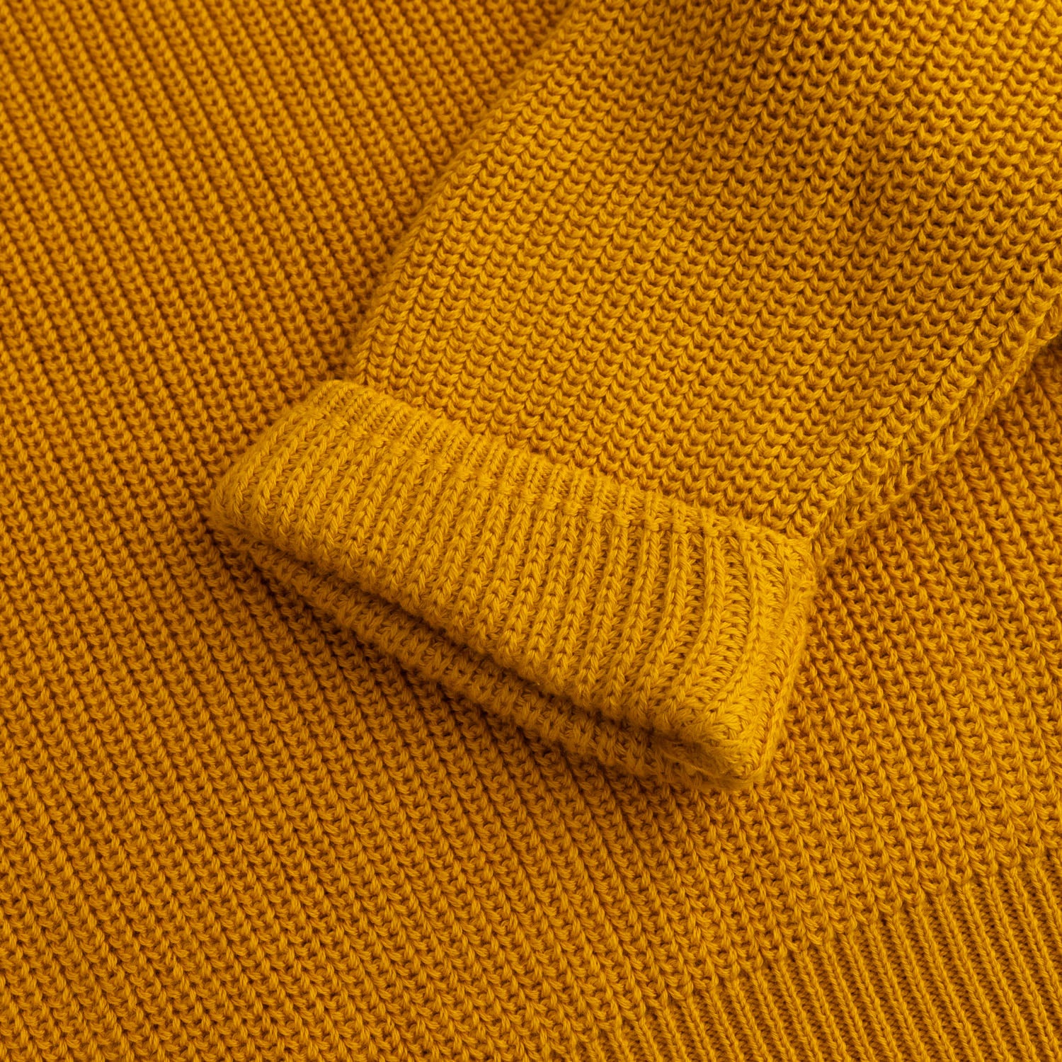 Close-up view of the soft textured mustard cotton fabric, folded sleeve cuff and ribbed hem of the girls knitted co-ord set.