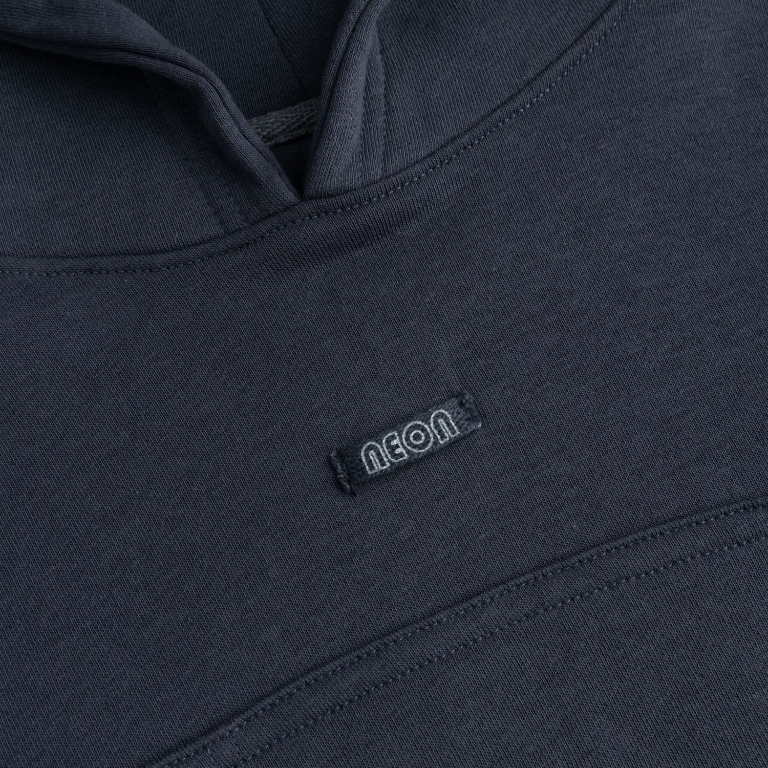 Close-up view of the soft charcoal grey fleece fabric, neatly finished hood neckline and subtle NEON logo detail on the girls pullover hoodie.