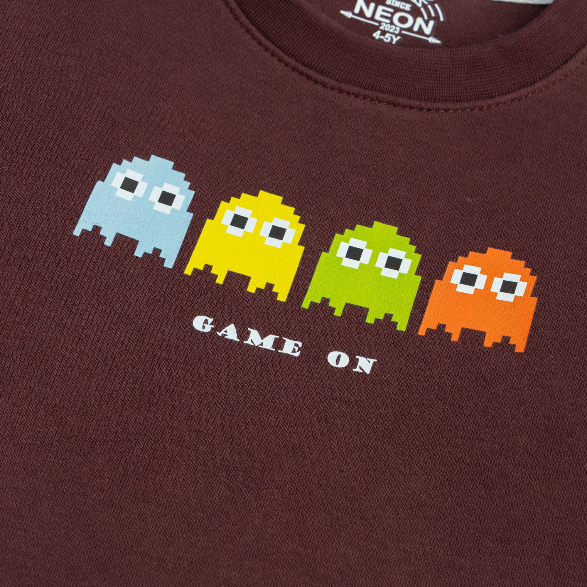 Close-up of the blue, yellow, green and orange pixel-style Game On graphic printed on the boys burgundy fleece sweatshirt.