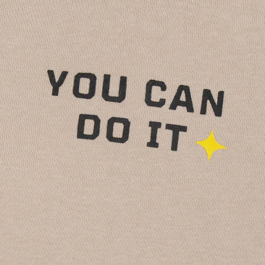 Close-up of the black You Can Do It text and yellow star graphic printed on the boys beige fleece sweatshirt.