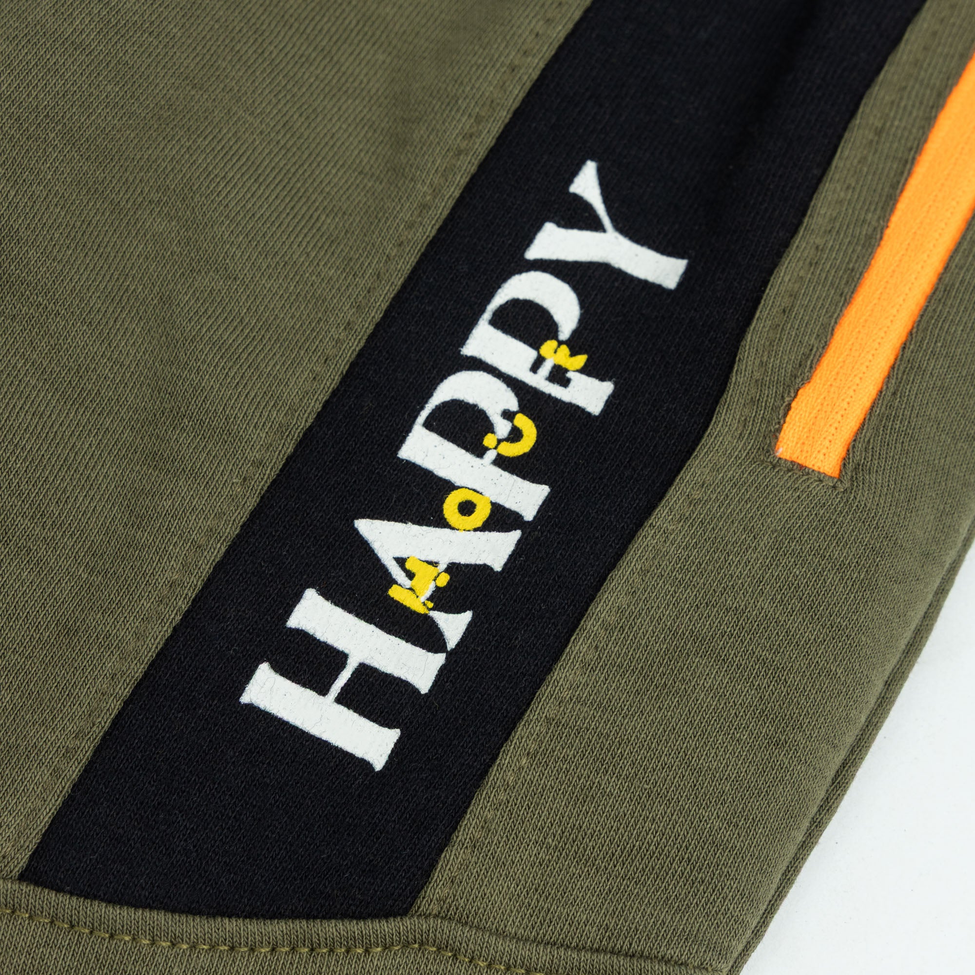Close-up of the “HAPPY” graphic, black contrast panel and orange zippered pocket on the boys olive green terry joggers.