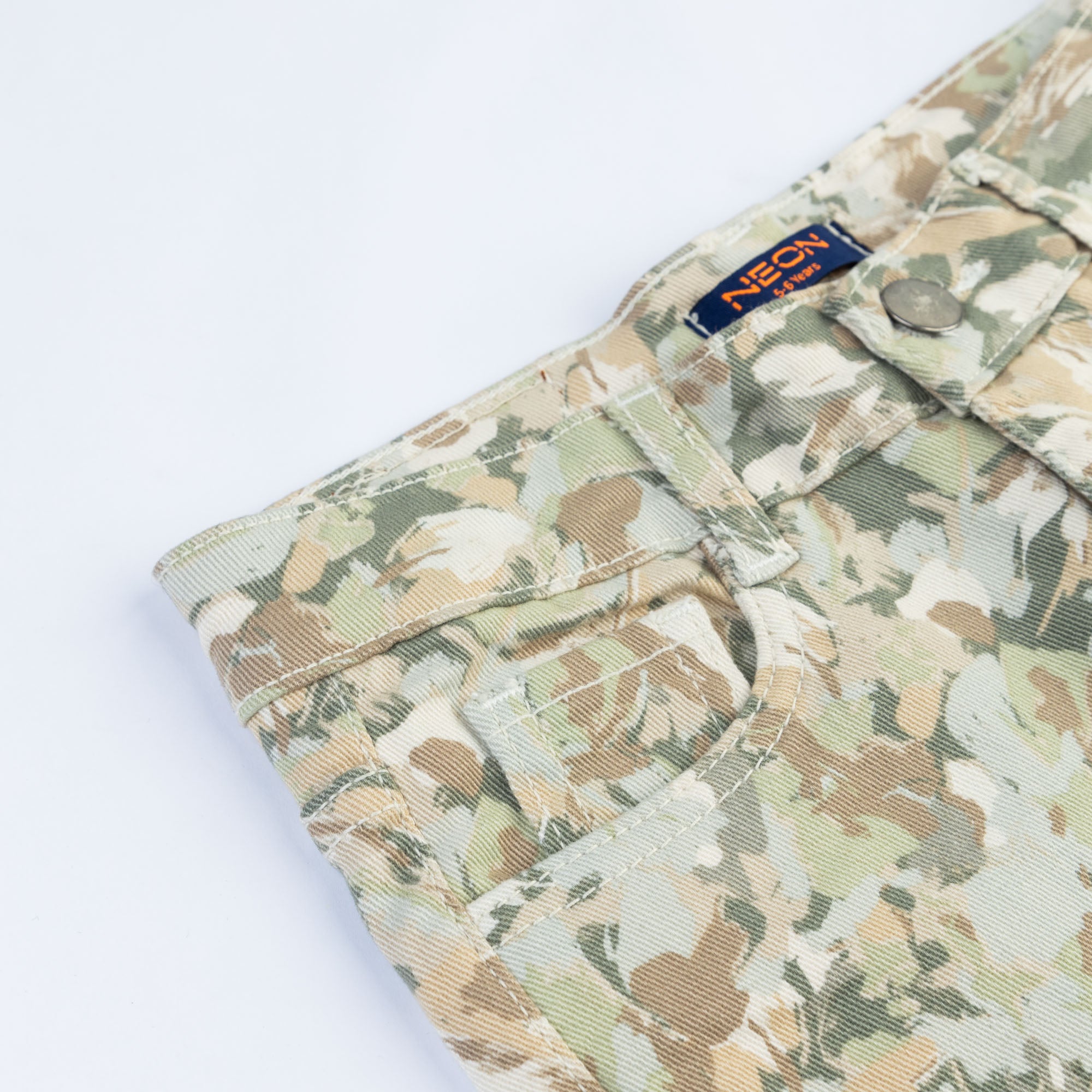 Close-up of the green camouflage pattern, front pocket, belt loops and button fastening on the boys’ printed pants.