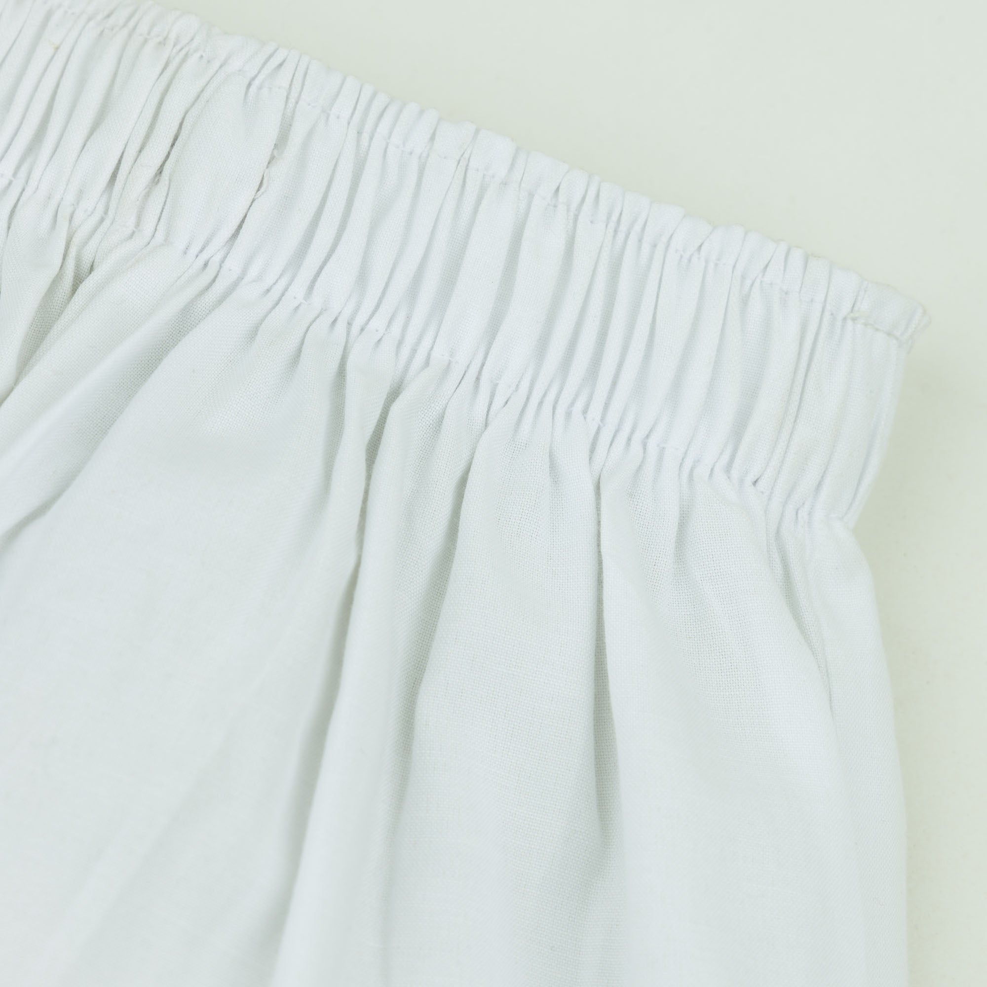Close-up of the fully elasticated waistband and lightweight woven texture of the boys off white cotton trousers.