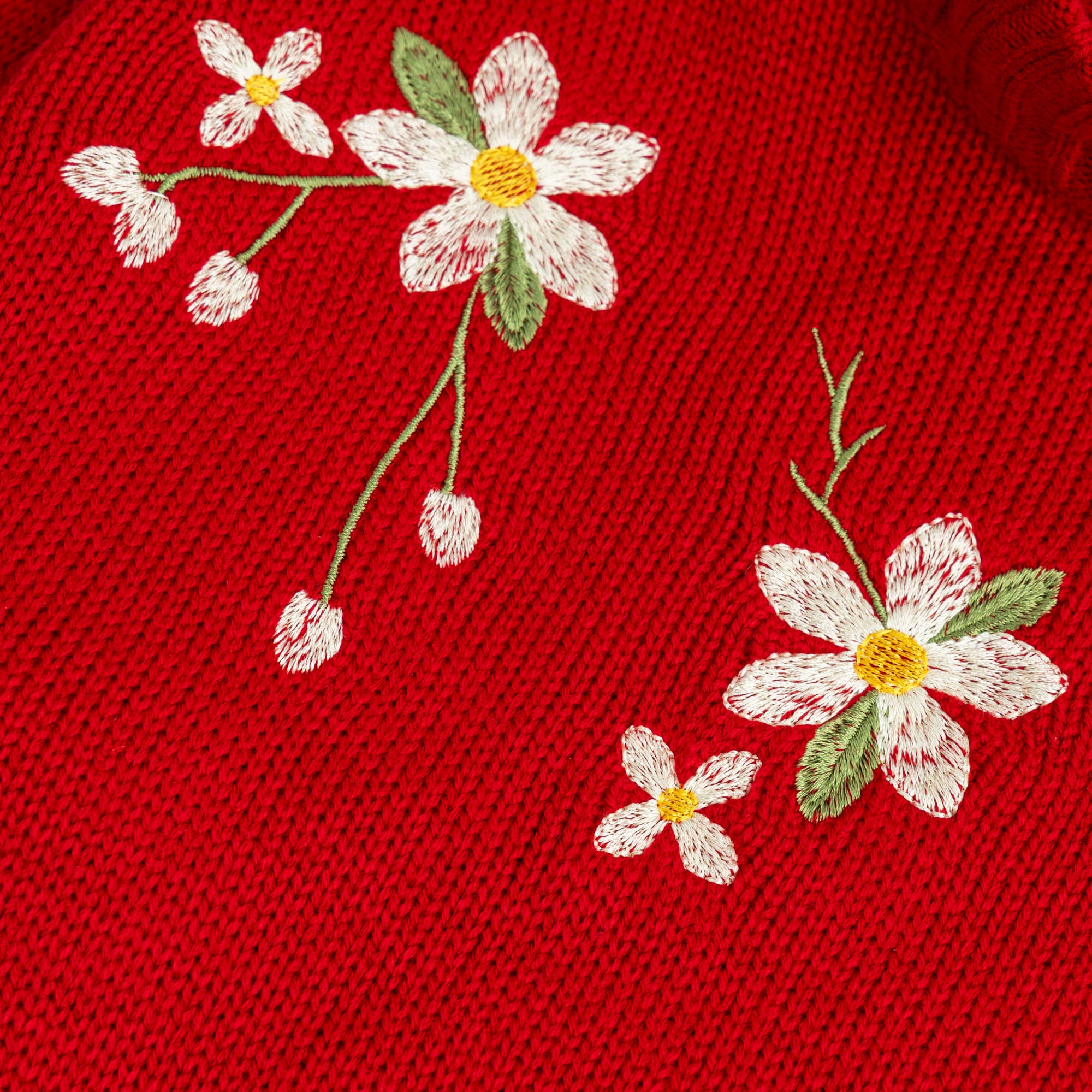 Close-up view of the ivory, sage green and yellow floral embroidery on the girls red acrylic sweater.