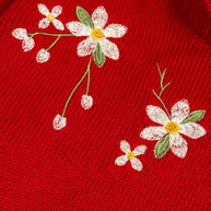 Close-up view of the ivory, sage green and yellow floral embroidery on the girls red acrylic sweater.