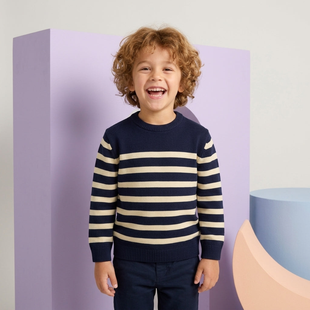 Smiling young boy wearing a navy and cream striped crew-neck sweater paired with navy trousers.