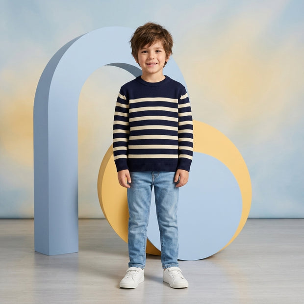 Young boy wearing a navy and cream striped crew-neck sweater paired with light-wash denim.