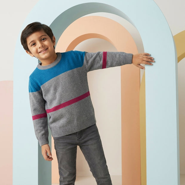 Young boy wearing a grey color-block sweater with blue and maroon stripe details, paired with charcoal denim.