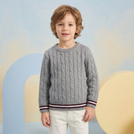 Young boy wearing a grey cable-pattern sweater with maroon and white striped trims, paired with white trousers.