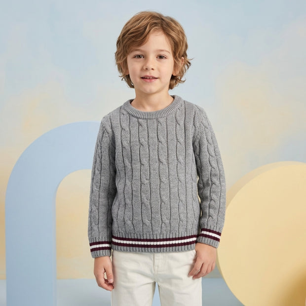 Young boy wearing a grey cable-pattern sweater with maroon and white striped trims, paired with white trousers.