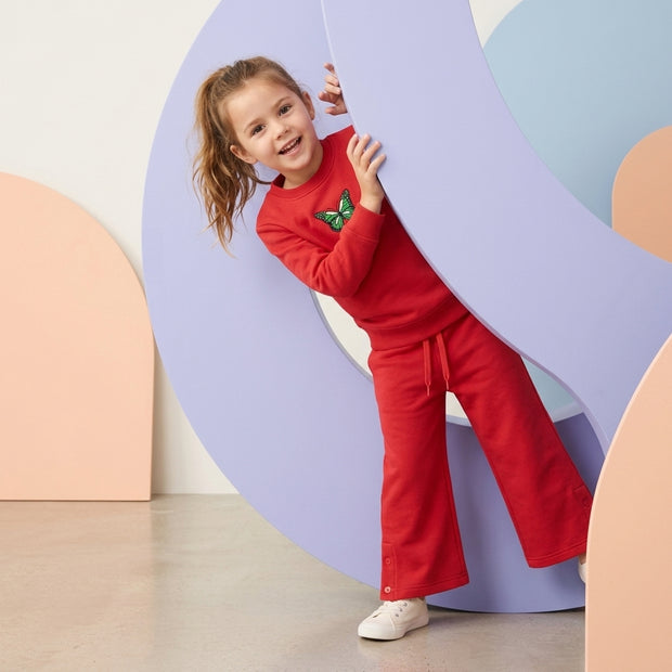 Girl wearing a red Butterfly Fleece Co-ord Set featuring a green butterfly graphic sweatshirt and matching flared trousers.