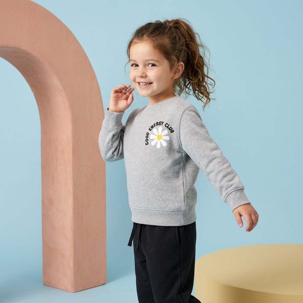 Young girl wearing a grey Good Energy Club fleece sweatshirt with a daisy graphic and black drawstring trousers.