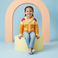 Smiling young girl wearing a multicolor button-down cardigan with a wide collar and front pockets, paired with light-wash denim.