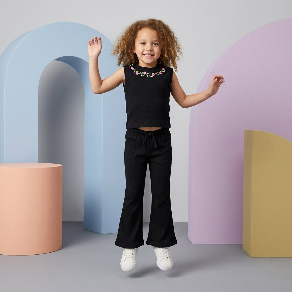 Smiling young girl wearing a black Floral Rib Co-ord Set with colorful floral embroidery and matching flared trousers.
