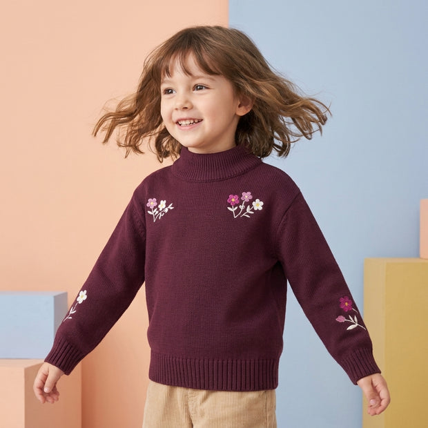 Smiling young girl wearing a burgundy floral embroidered mock-neck sweater with ribbed trims.