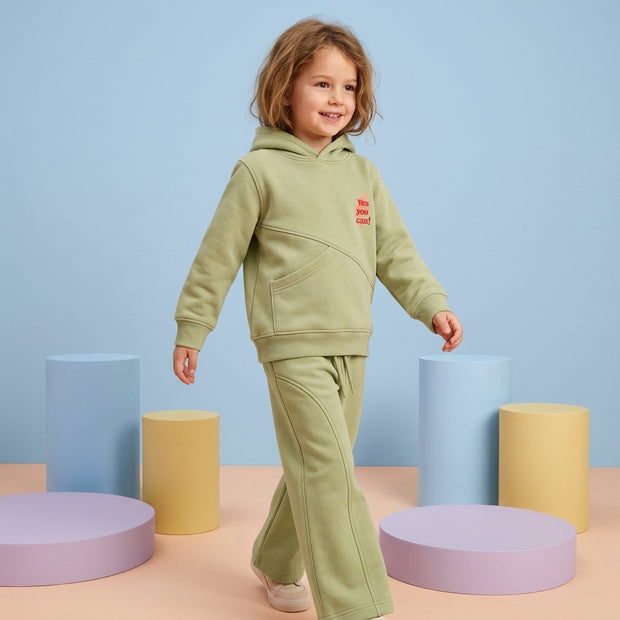 Smiling young girl wearing a sage green fleece co-ord set with a hooded sweatshirt and matching wide-leg trousers.