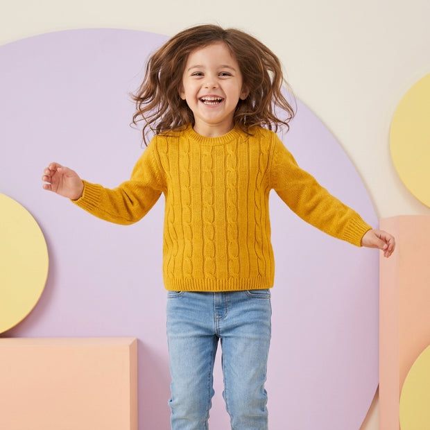 Smiling young girl wearing a mustard cable-pattern sweater paired with light-wash denim.