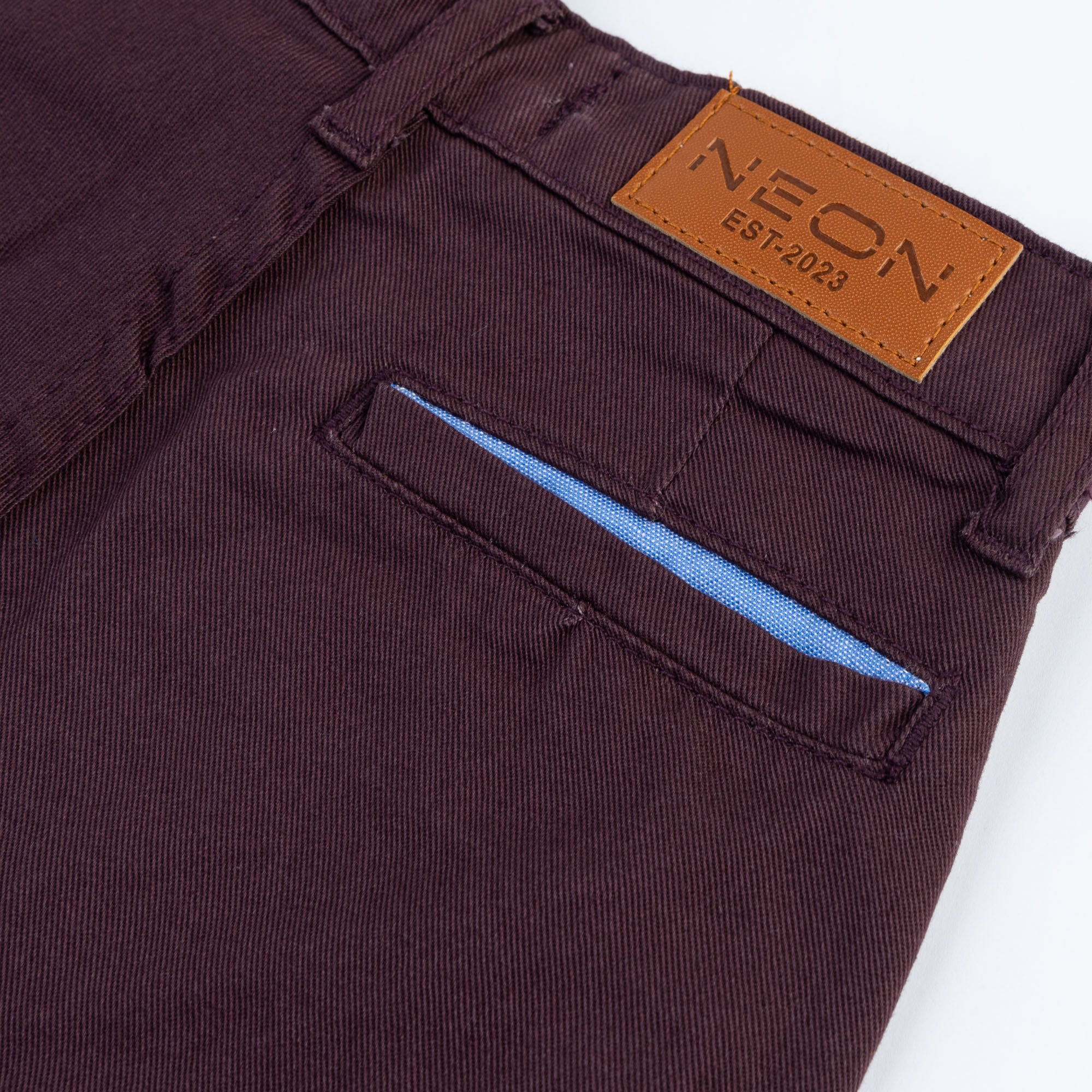 Close-up of the back welt pocket, blue lining and branded tan waist patch on the kids dark plum twill pants.