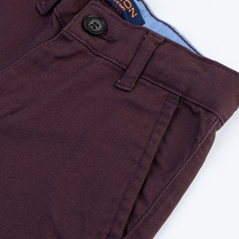 Close-up of the button fastening, belt loop, slanted pocket and twill texture on the kids dark plum pants.